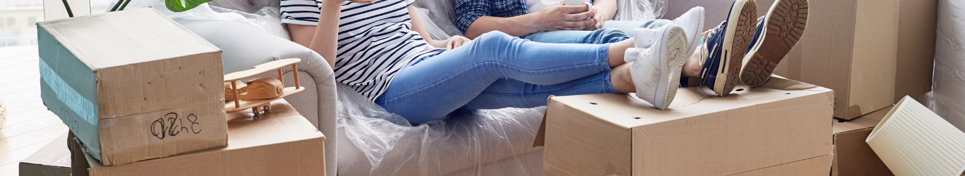 moving boxes, two people sitting couch with feet on box