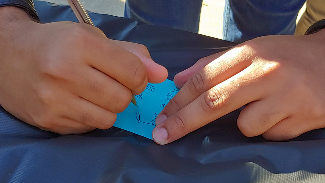 Student writing on a blue Postit note