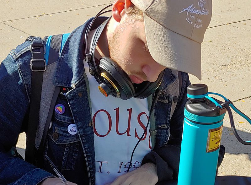 student writing at table with water bottle